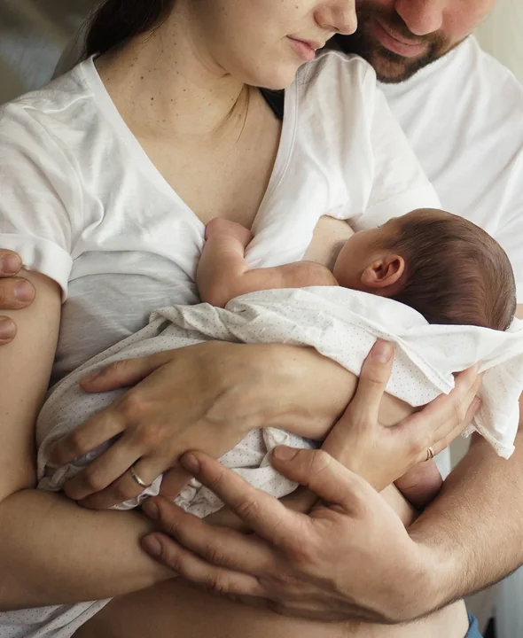 A mother breastfeeding her newborn, held by her partner